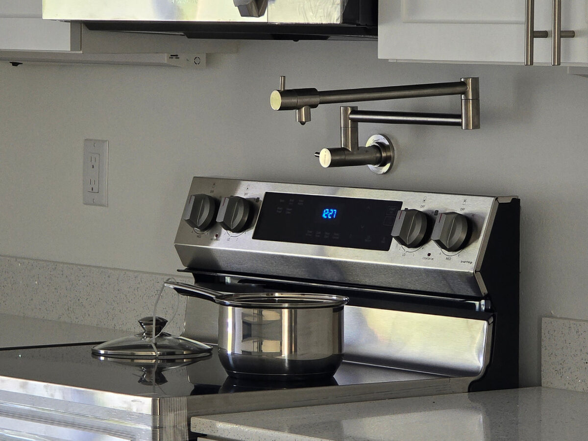 Wall-mounted pot filler faucet above stove with stainless steel appliances