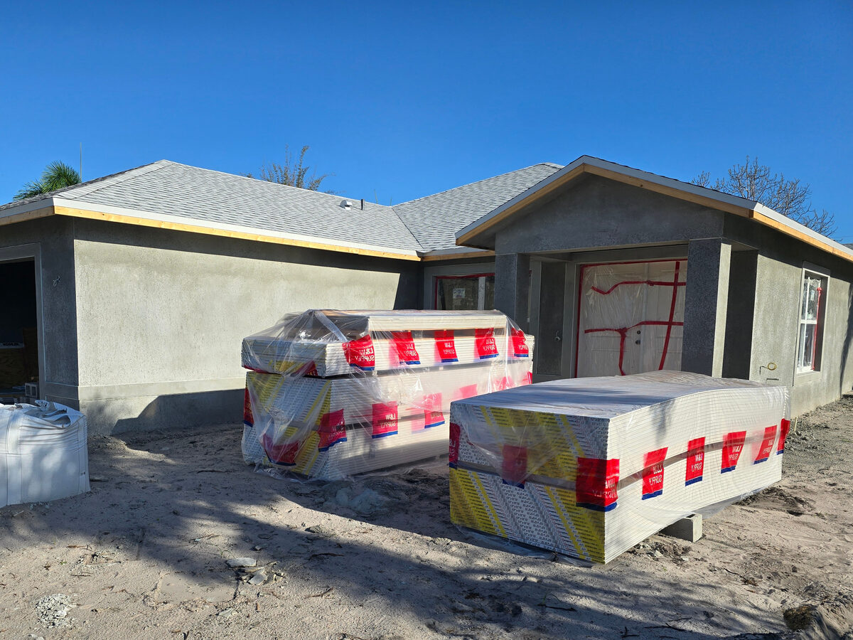 Stucco applied to exterior walls — drywall materials staged inside