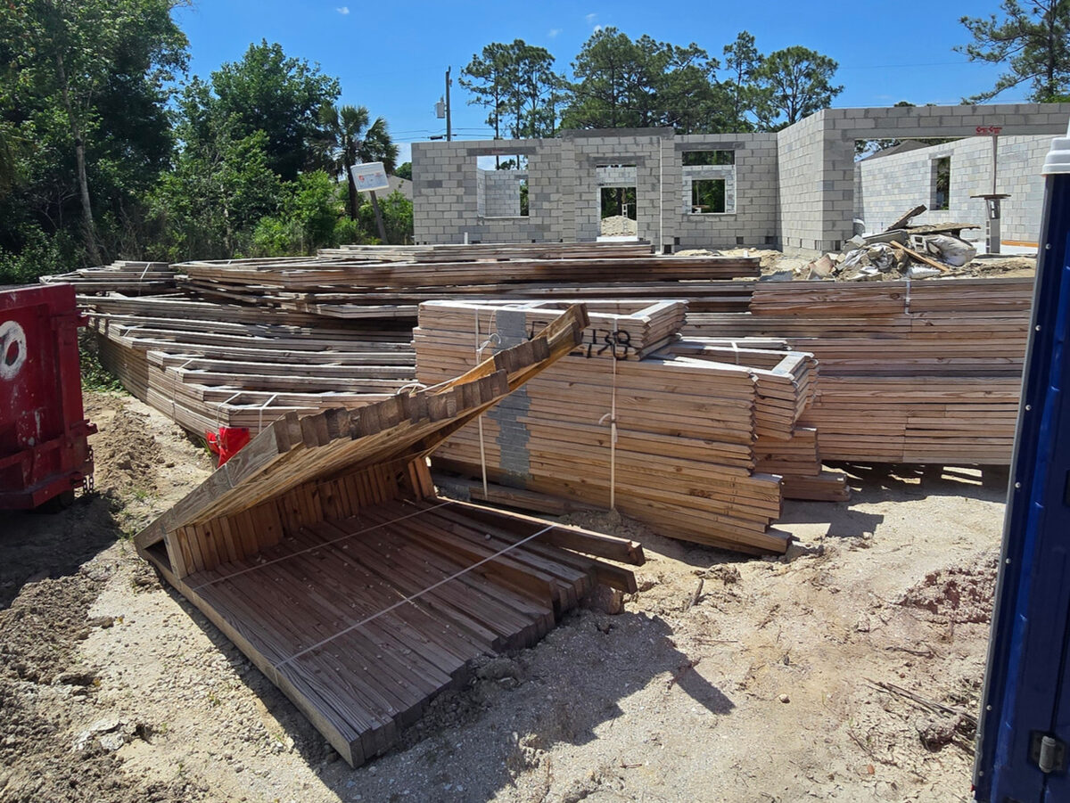 Lumber packages delivered and staged on site with block structure in background
