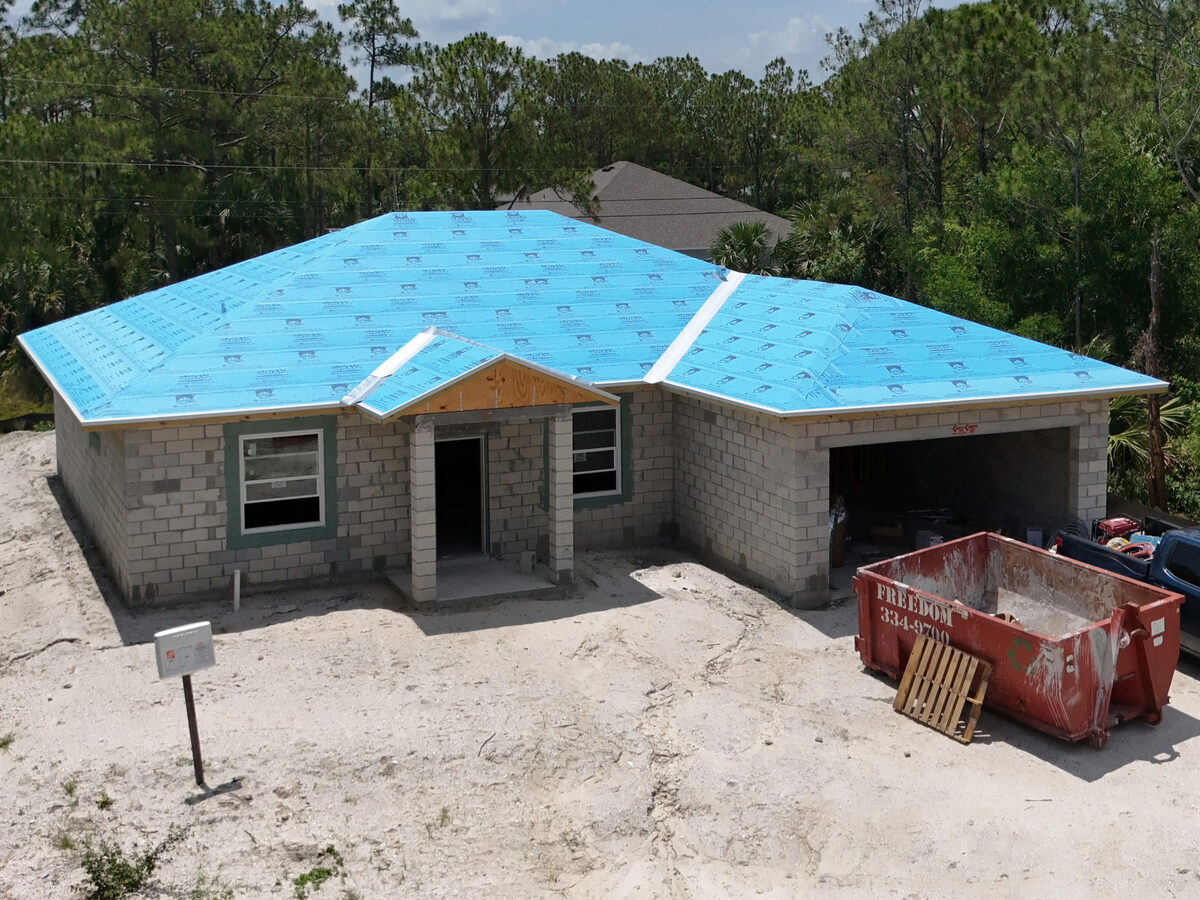 Drone side view of home with underlayment and dumpster on site