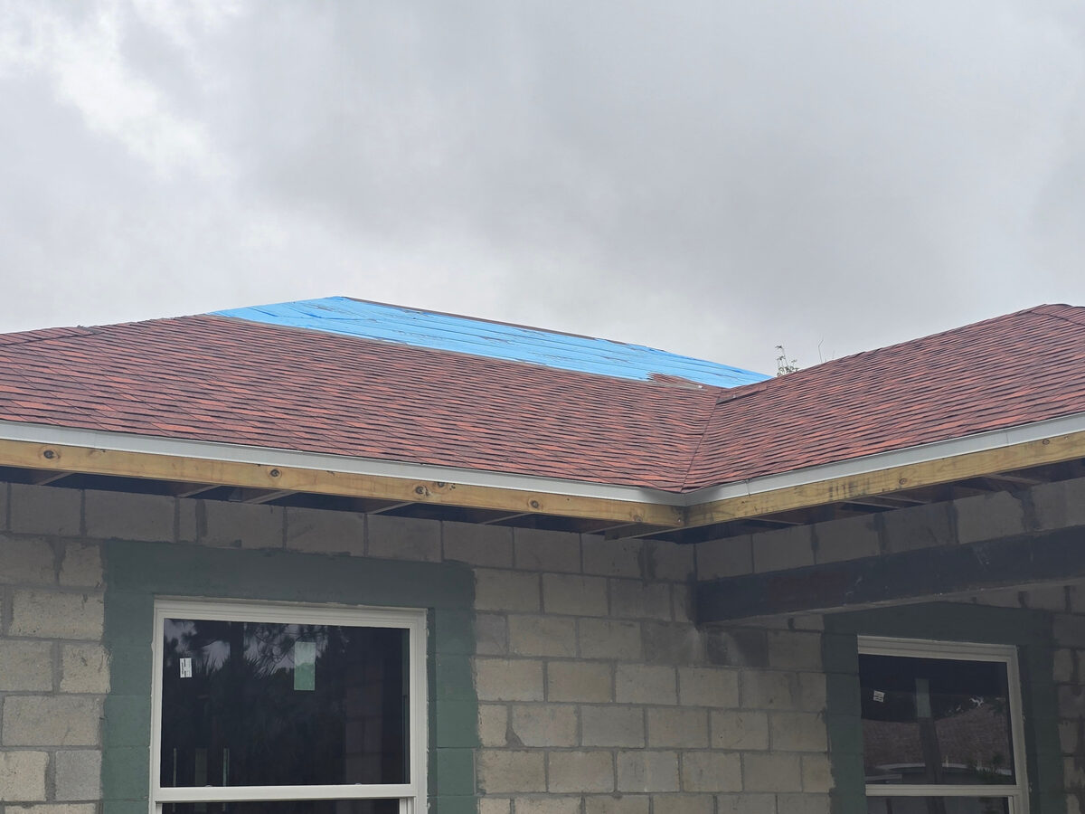 Close-up of shingle installation with blue underlayment still visible at ridge