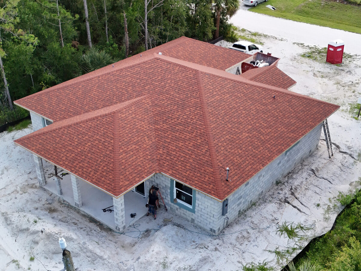 Aerial view of completed shingle roof — front angle with workers at entry