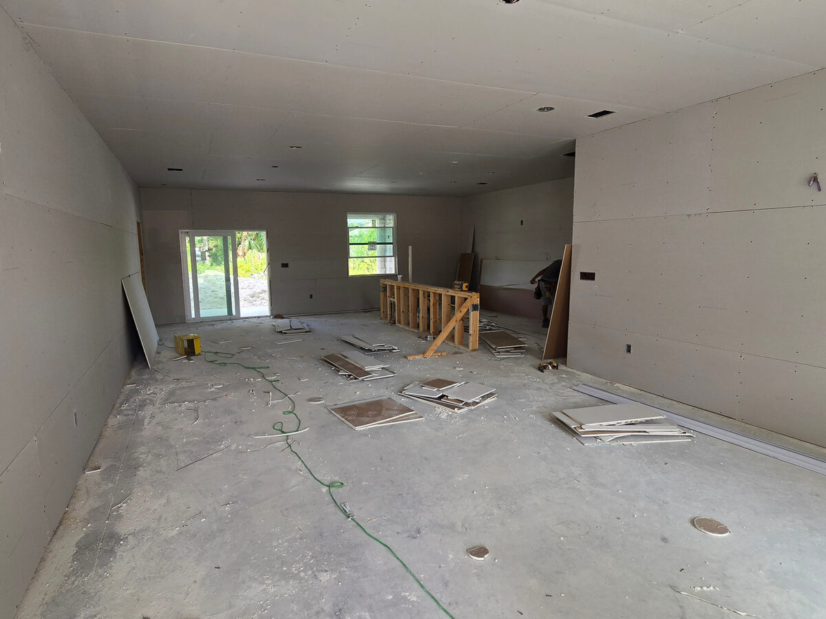 Drywall sheets being hung with kitchen island framing and materials on floor