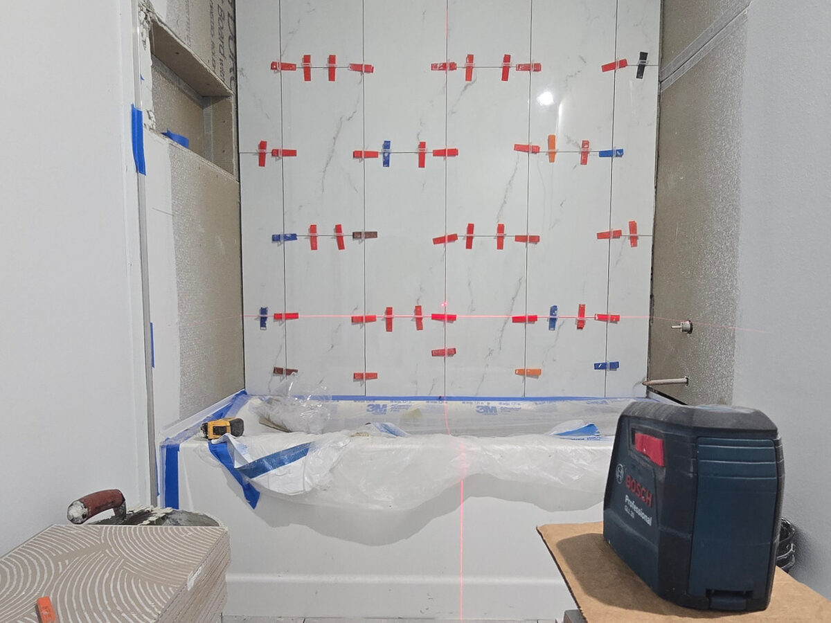 Marble-look wall tile installation in bathroom with laser level for precision alignment