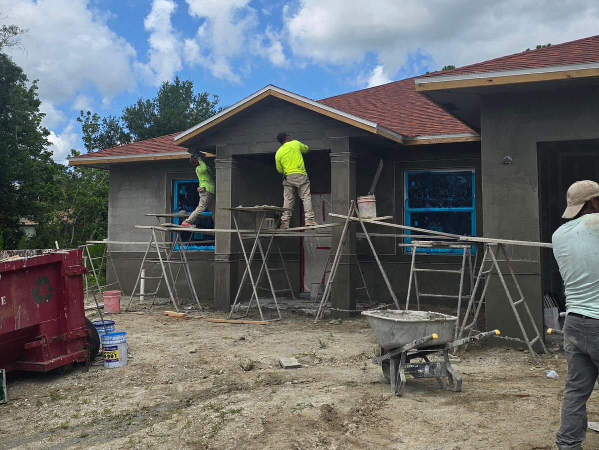 Workers applying stucco on scaffolding — front elevation with entry columns