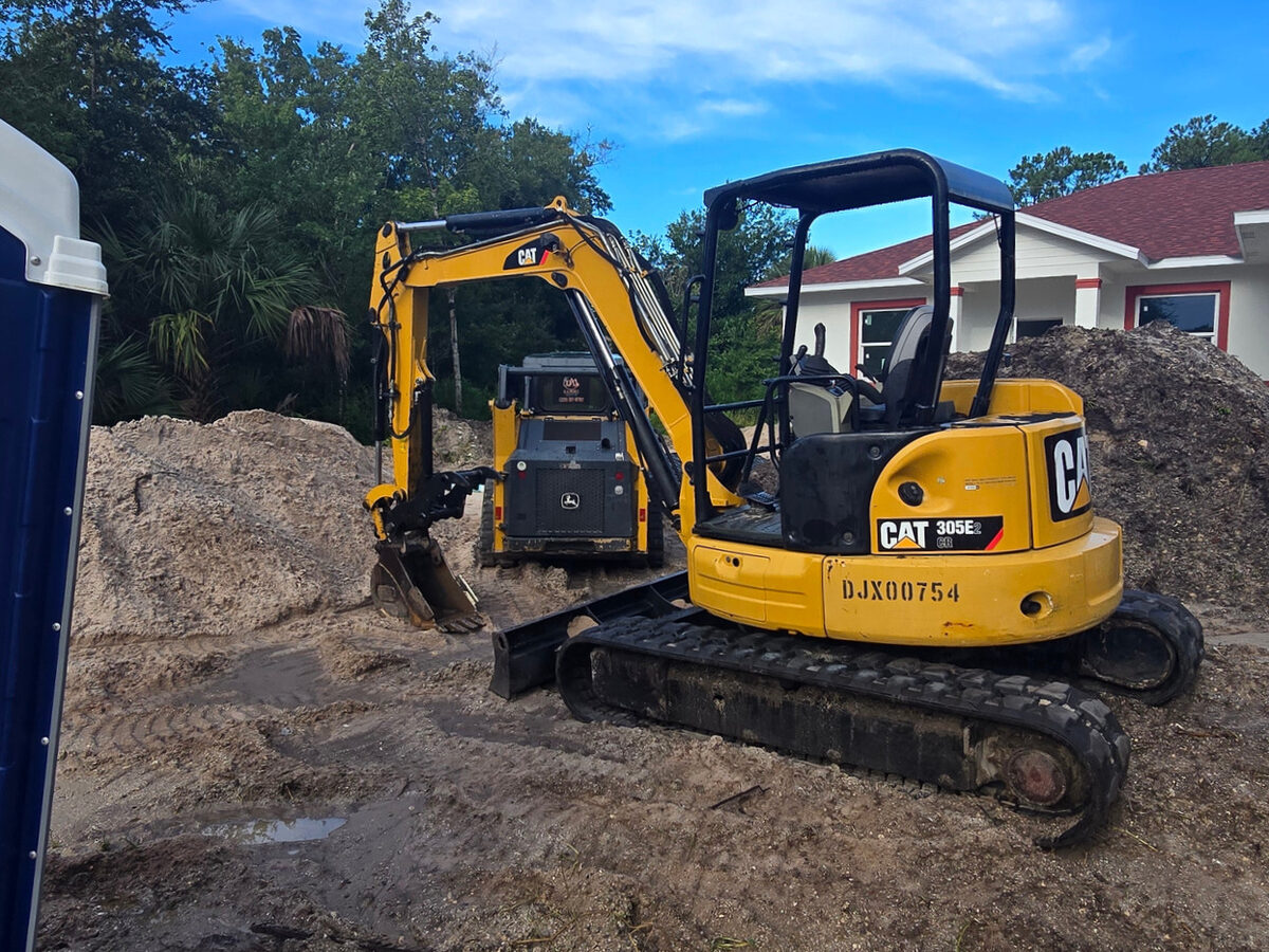 CAT excavator grading the site with painted home visible in background