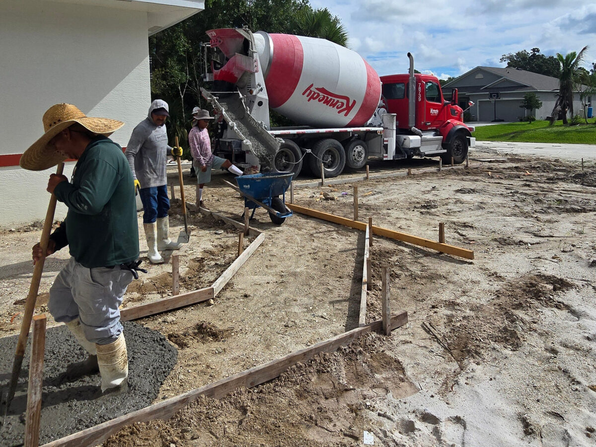 Concrete mixer truck and crew pouring the driveway with formboards in place