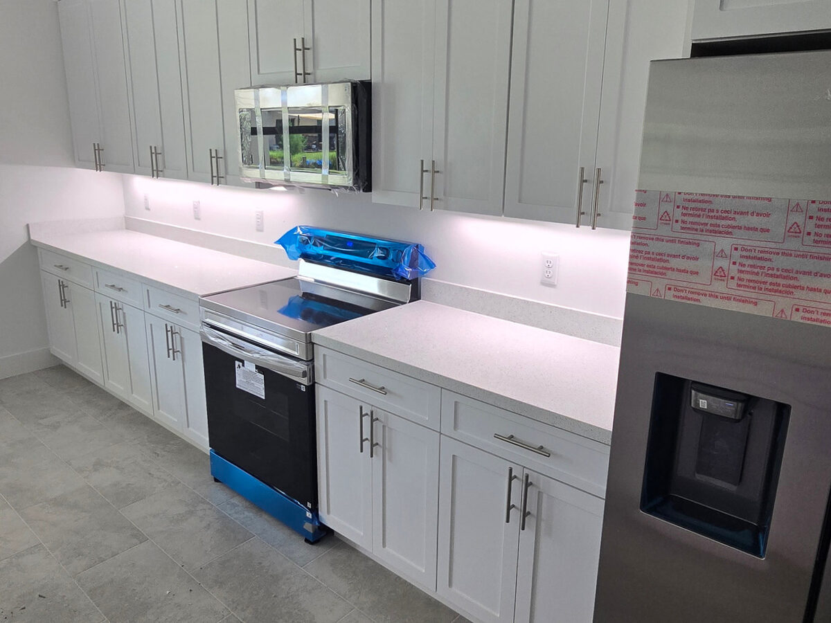 Kitchen wall cabinets with LED under-cabinet lighting, stainless steel appliances with protective film