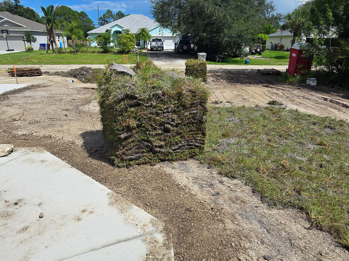 Sod pallets stacked and ready for installation at the driveway with neighborhood visible