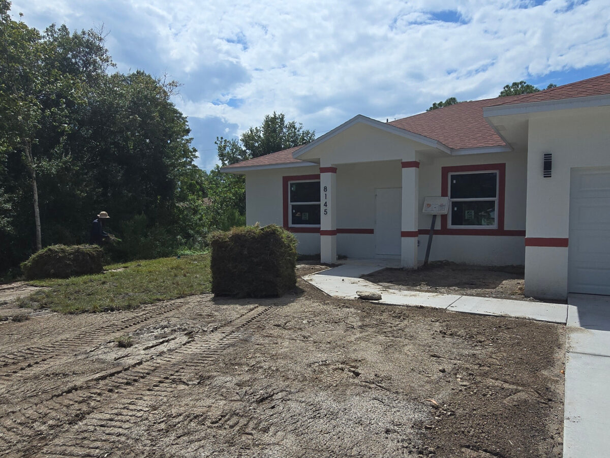 Worker laying sod at the front yard with painted home and entry porch visible