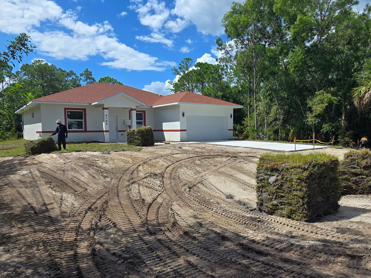 Full front view of home with sod partially installed, driveway complete and workers on site