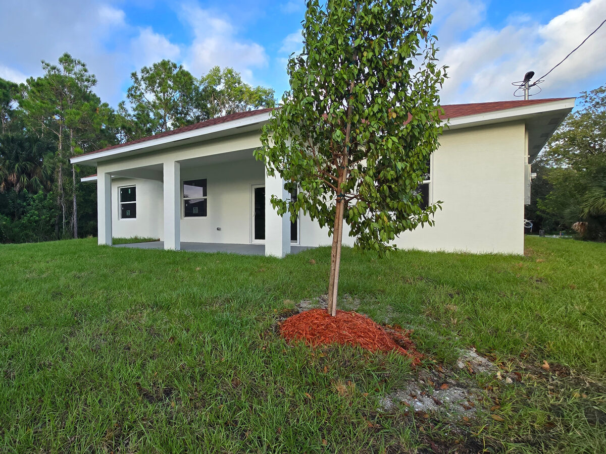 Rear view with covered lanai, planted tree with mulch ring and fresh green lawn