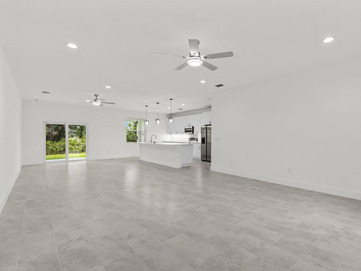 Same open-concept living area unfurnished — clean tile floors, ceiling fans and recessed lighting