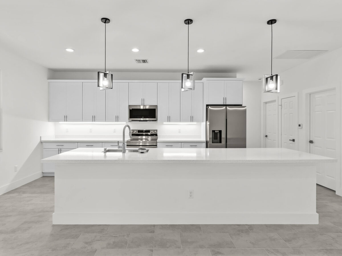 Professional photo of kitchen — white shaker cabinets, quartz island, pendant lights and stainless appliances