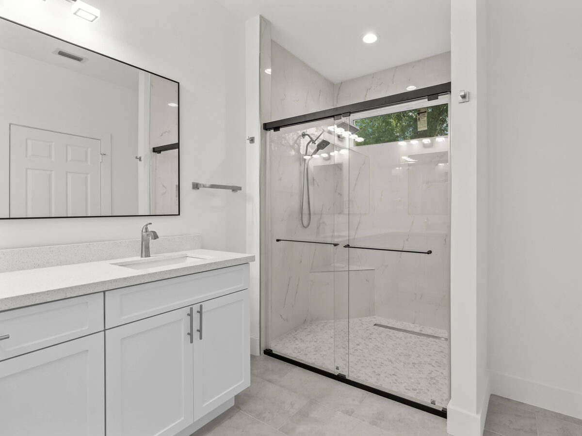 Guest bathroom with glass sliding shower, marble-look wall tile, pebble floor and white shaker vanity