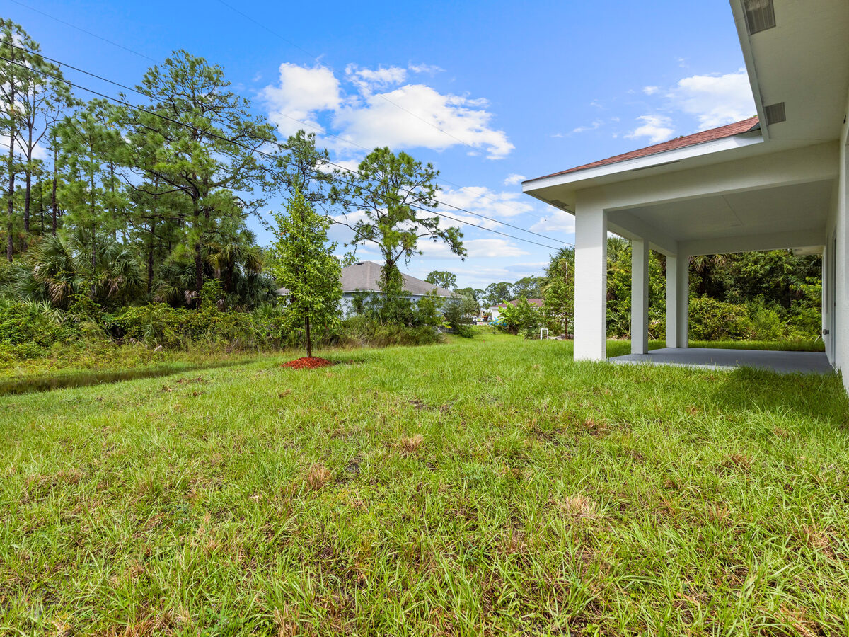 Backyard with covered lanai, planted tree with mulch ring and lush green lawn